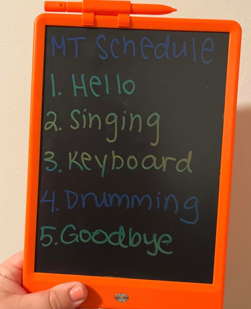 Orange LCD tablet with Abby's writing: MT schedule/hello/singing/keyboard/drumming/goodbye