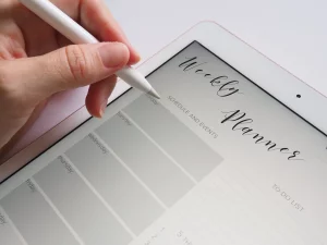 hand with apple pencil hovering over of a white iPad that displays a digital weekly planning page.