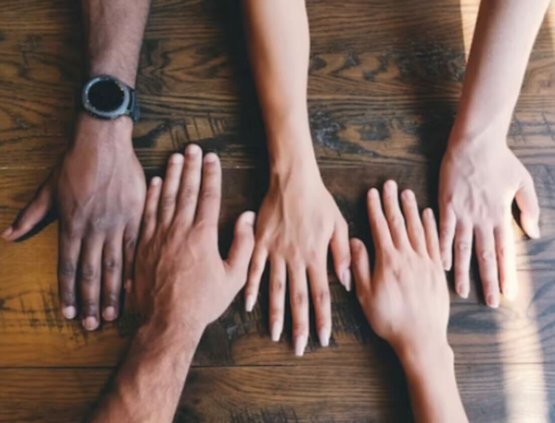 Hands of varying skin tones laying flat on a wooden table